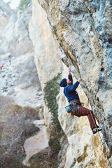 Obraz premium male rock climber climbs on a rocky wall at winter sunny day. Man climber in warm clothes on yellow cliff.