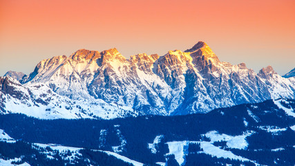 Panoramic view of winter mountains. Alpine peaks covered by snow and illuminated by rising sun.