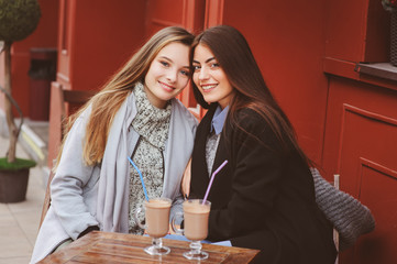 two happy girl friends talking and drinking coffee in autumn city in cafe. Meeting of good friends, young fashionable students with natural make up.