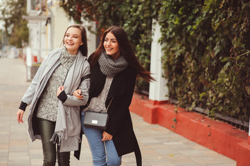 two young happy girlfriends walking on city streets in casual fashion outfits, wearing warm coats and having fun
