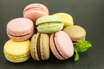 french sweet macarons  in pink, yellow, green and brown with mint on slate plate