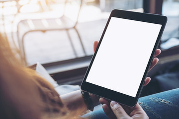 Mockup top view image of a woman sitting cross legged and holding black tablet pc with blank white screen on thigh in cafe