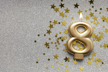 Number 8 gold celebration candle on star and glitter background