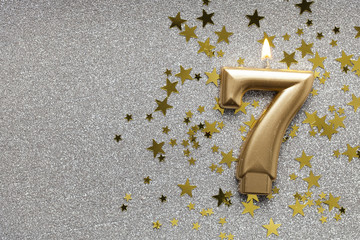 Number 7 gold celebration candle on star and glitter background