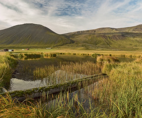 A small lake against a background of green hilly mountains. Traditional landscape of Iceland. Beautiful northern landscape.
