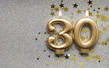 Number 30 gold celebration candle on star and glitter background
