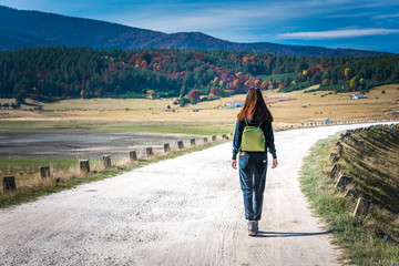 A girl walking down the road with a green backpack in Rhodope mountains Bulgaria in Autumn.