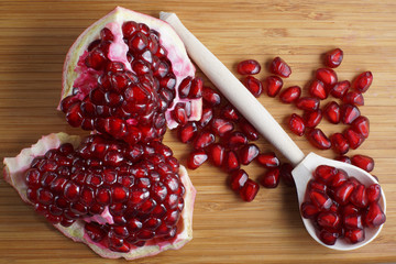 Red pomegranate seeds lie on a wooden spoon next to a piece of pomegranate. Ripe seasonal fruits