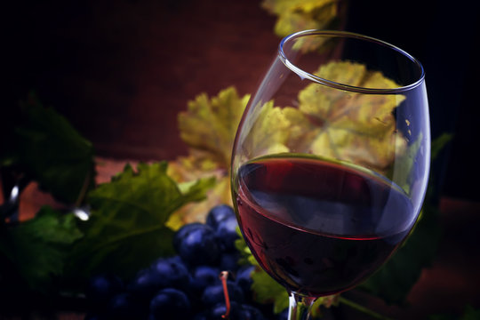 Red wine from grape varieties merlot in glass, vintage wooden background, selective focus