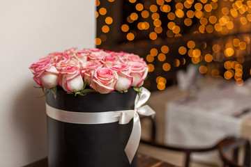 A bouquet of roses in a hat box in a dark room against the background of bokeh lights