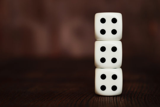 Three white plastic dices column on dark brown wooden board background. Six sides cube with black dots. Unlucky number four - 4. Tetraphobia concept.