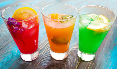 Different kinds of fresh lemonades in glasses and glass of water with lemon on light background