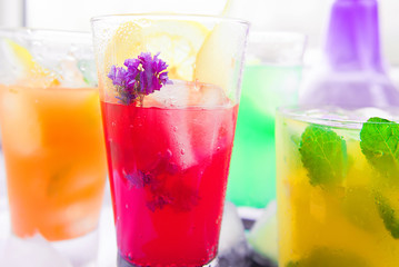 Different kinds of fresh lemonades in glasses and glass of water with lemon on light background