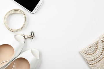 Female white shoes, belt, smartphone and bag on a white background top view, flat lay