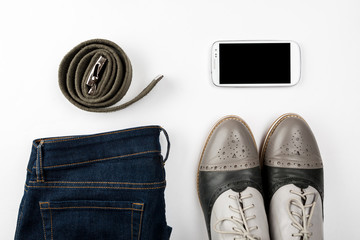 Belt, blue jeans, white smartphone and gray shoes on a white background top view, flat lay