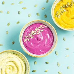 bright appetizers in the form of sauces on a blue background among pumpkin seeds. Hummus, carrot and beetroot sauces. Top view. Flat lay