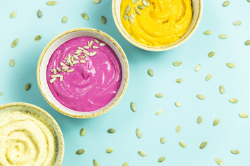 bright appetizers in the form of sauces on a blue background among pumpkin seeds. Hummus, carrot and beetroot sauces. Top view. Flat lay. Copyspace