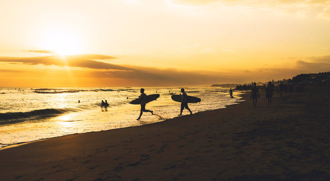Beautiful seascape at the nightfall with silhouettes of surfers. A sunset at the tropical sand beach. Surfers are spending summer vacation riding at the tropical country with good waves.