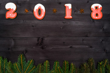 Happy new year 2018 sign symbol from red and white gingerbread cookies on dark wooden background with fir tree branches, copy space. Top view, flat lay. New Year or Christmas postcard