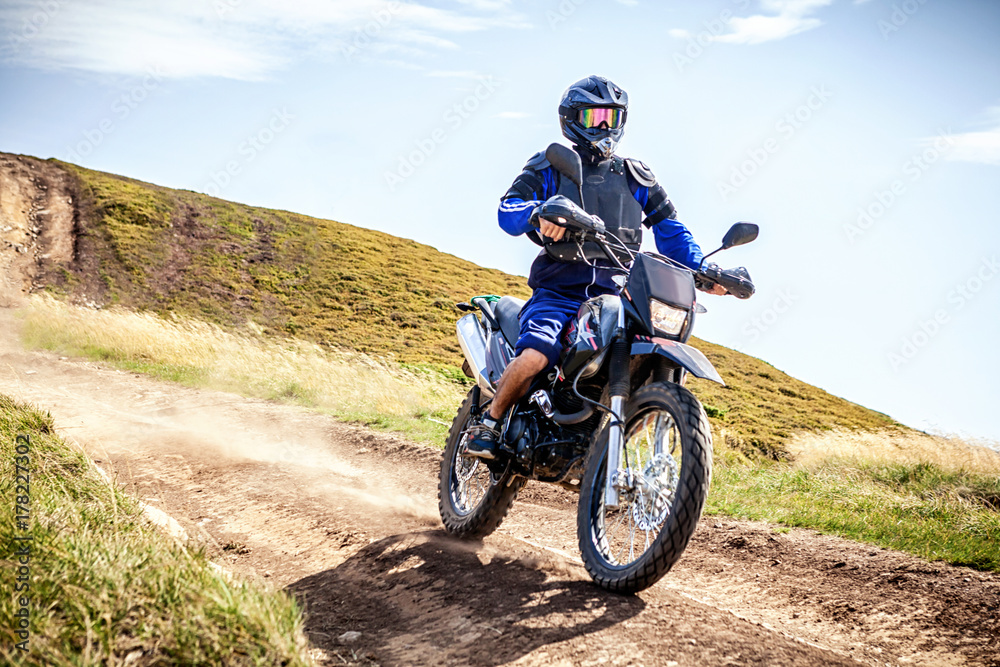 Wall mural Enduro biker crossing road at high speed in Carpathian mountains.