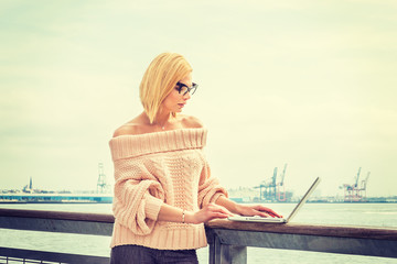 Eastern European Business Woman traveling, working in New York. Wearing sweater, glasses, American college student reading, working on laptop computer by river. Copy Space. Instagram filtered effect.