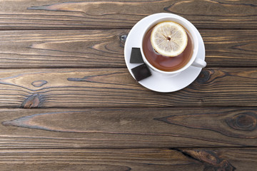 cup of tea with lemon, two slices of chocolate on a wooden background