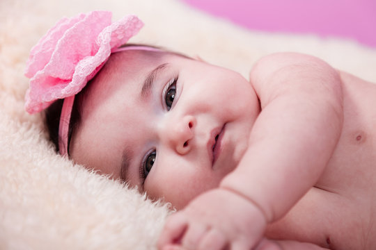 Cute, pretty, happy, chubby baby girl portrait, without clothes, naked or nude, on a fluffy blanket. Pink flower headband. Looking at camera. Four months