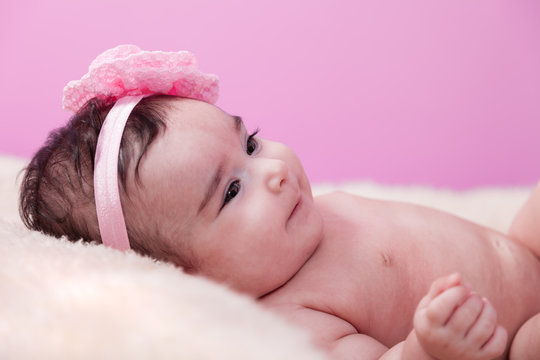 Cute, pretty, happy, chubby baby girl portrait smiling with a big smile. Lying naked or nude on fluffy blanket. Pink flower headband. Four months old