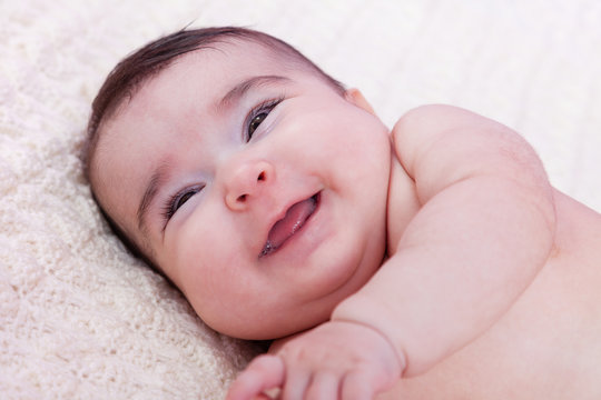 Cute, pretty, happy, chubby and smiling baby girl portrait, laughing with a big smile. Naked or nude on fluffy blanket. Four months old
