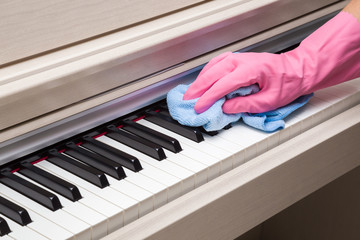 Employee's hand in rubber protective glove with rag wiping a piano keys. Cares about musical instruments. General or regular clean up. Commercial cleaning company concept.
