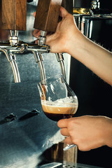 Hand of bartender pouring a large lager beer in tap.