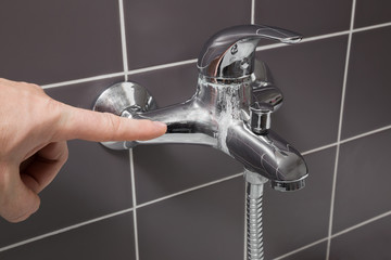 Man's hand finger pointing to calcified water tap in the bathroom. Problem concept.