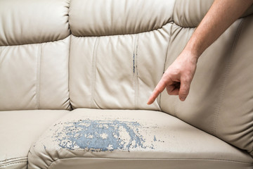 Man's hand finger pointing to sofa damaged leather. Problem concept.