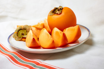 The persimmon and sliced fruit are on a plate.