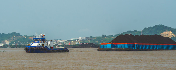 tugboat pulling heavy loaded barge of coal cruising Mahakam River in Samarinda, Indonesia