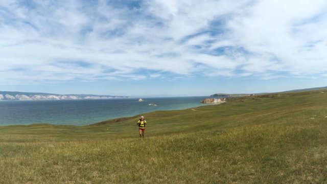 Woman hiker trekking on walking along blue lake. Wearing backpack. Healthy lifestyle Caucasian girl in Siberia in summer, Russia