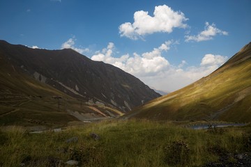 Горный пейзаж, красивый вид на живописные склоны, солнечная погода, белые облака на синем небе, горы и природа Кавказа