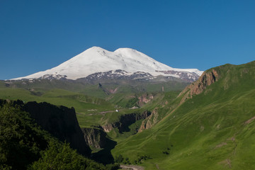Mount Elbrus in the summer in the snow and green grass around
