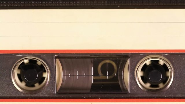 Macro static camera view of vintage audio cassette tape with a blank white label in use sound recording in a cassette player. Cassette Tape with a white blank label