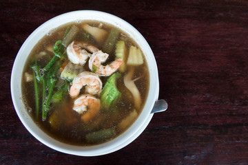 Spicy vegetable and prawn soup in bowl on wooden table