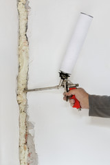 Worker fixing hole in wall using polyurethane expanding foam glue gun applicator
