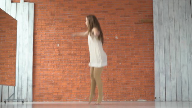 A professional dancer dances in the ballroom in front of a mirror. a woman is tumbling on the floor. young attractive girl is exercising indoors on the background of a kerf wall. the woman is wearing
