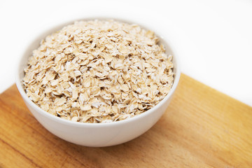 oat flakes in a white bowl on cutting board on a white background
