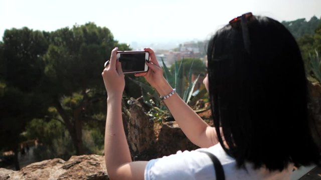 Beautiful brunette tourist woman in sunglasses enjoy and take photo with mobile phone smartphone in tropical resort. Travel concept. Park Guell in Barcelona. Dolly shot. Slow motion.