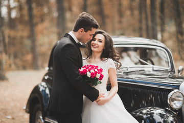 Beautiful wedding couple posing near splendid retro car