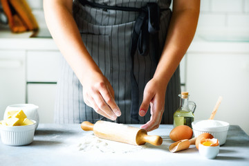 Female hands kneading dough, baking background. Cooking ingredients - eggs, flour, sugar, butter, milk, rolling pin on white style kitchen. Copy space