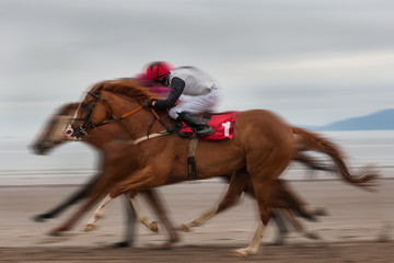 Speeding race horses and jockeys running on the beach, motion blur effect