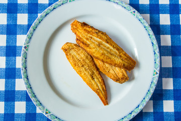 three small fried dover sole fish on white plate with blue and white table cloth