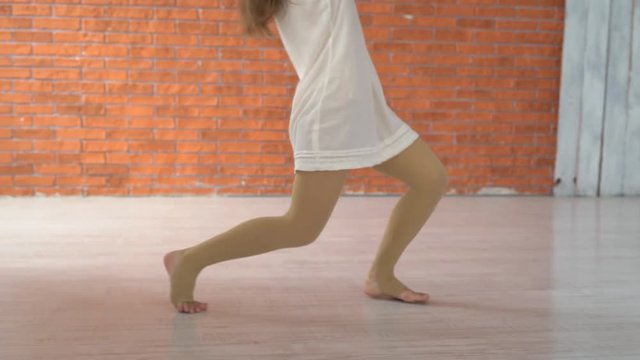 A professional dancer dances in the ballroom in front of a mirror. a woman is tumbling on the floor. young attractive girl is exercising indoors on the background of a kerf wall. the woman is wearing
