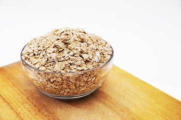 oat flakes in a transparent bowl on cutting Board on white background